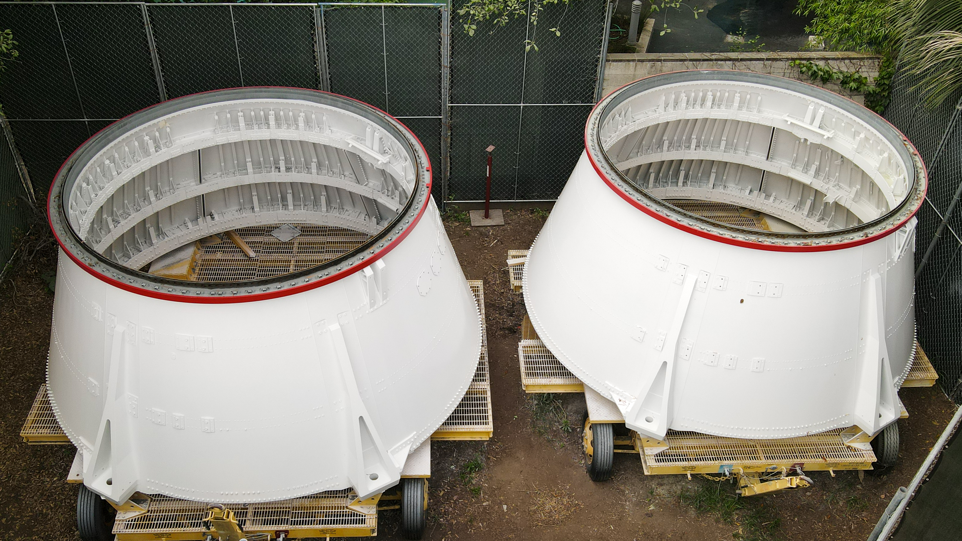Two huge metal cylindrical structures, painted white, sitting on rolling dolly's in a storage area