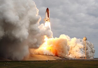 Space shuttle Endeavour roars off the launch pad in a cloud of steam and smoke.