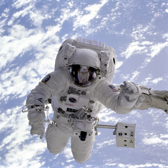 An astronaut conducts a spacewalk with Earth visible behind him.