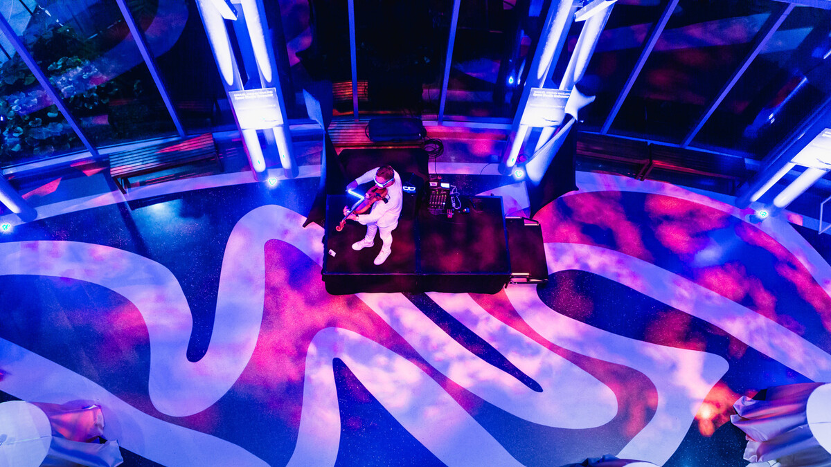 violinist plays on stage in Ecosystems atrium lit in electric blue