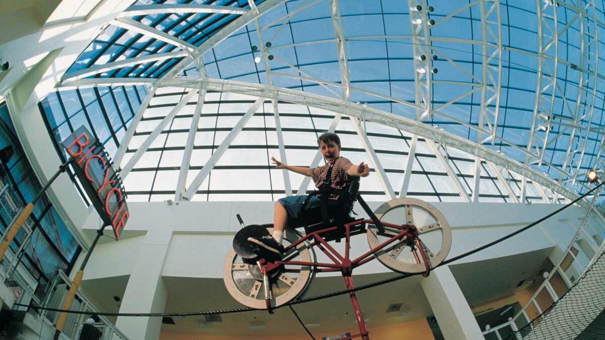 Aided by physics, a boy with outstretched arms balances a bike on a wire.