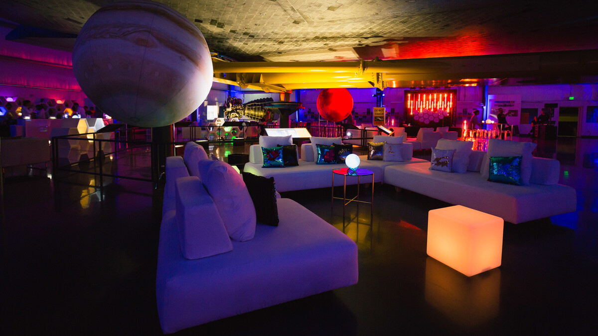 Closeup under the belly of the Space Shuttle Endeavour of white lounge furniture, neon room accents, and planetary airstars
