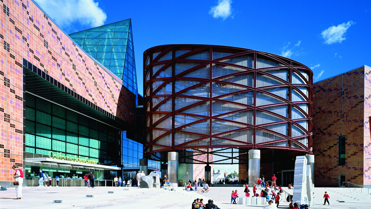 Exterior photo of the California Science Center building with crowds in the distance.