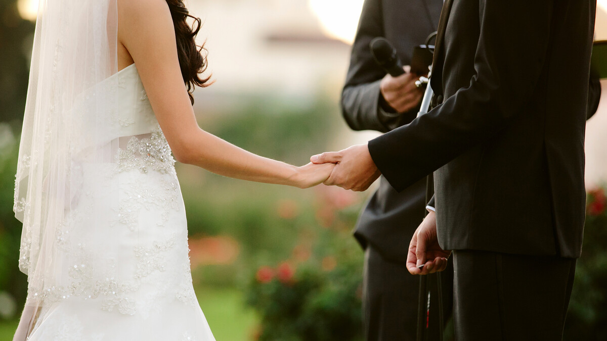 Bride and groom hold hands during wedding ceremony in the Exposition Park Rose Garden