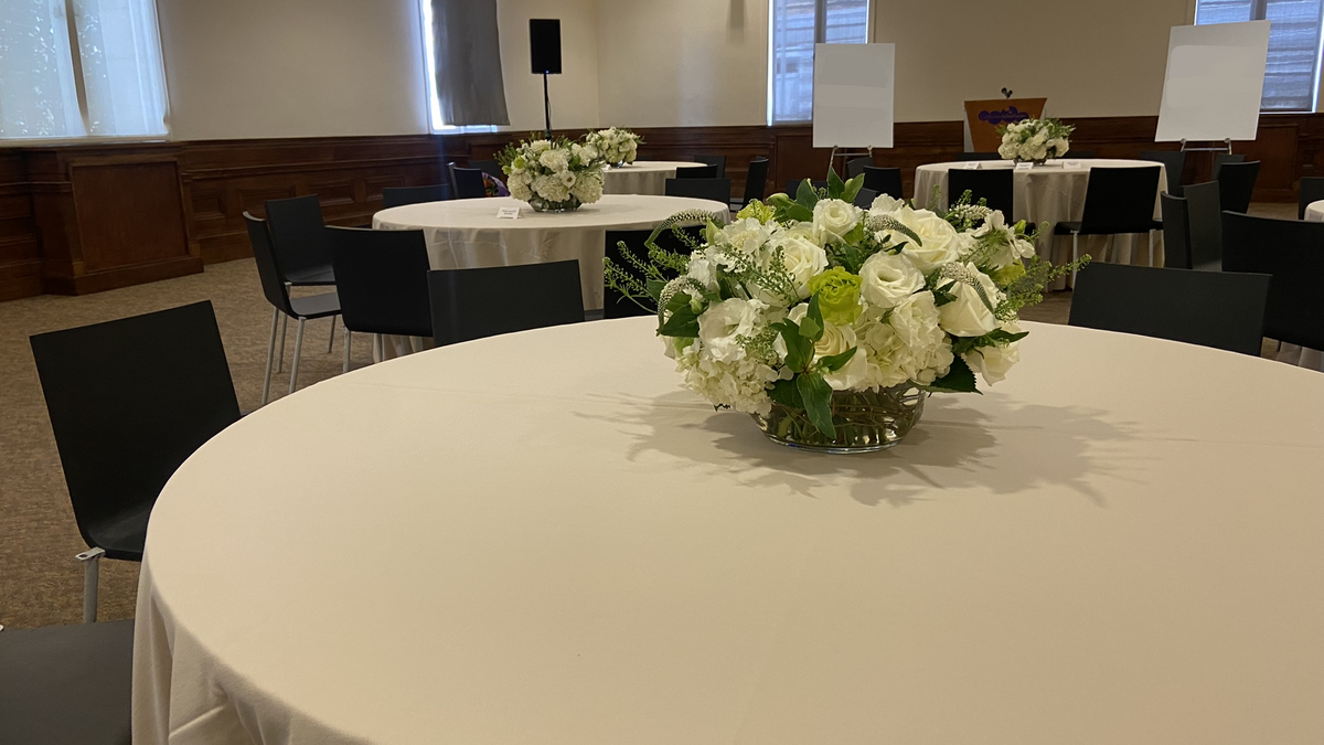Muses Room set for an intimate luncheon and presentation with 3 round tables topped with cream linens and white and green florals