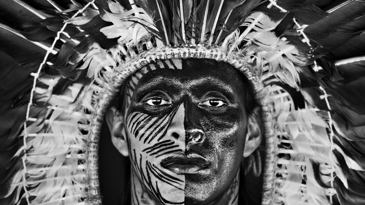 Adão Yawanawá in a headdress of eagle feathers, wearing face paint made from the fruit of the genip tree.