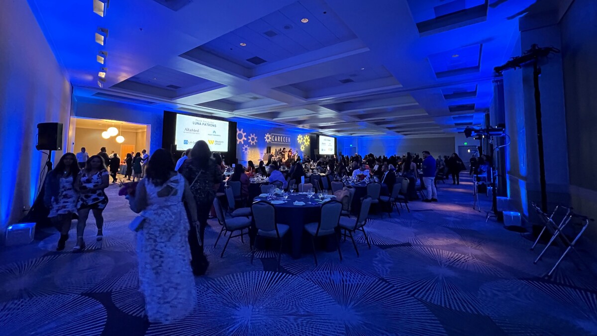Guests are seated for a gala in the Loker Conference Center. The event space is flanked by large programmatic screens and the room has a blue-hue from event lighting.
