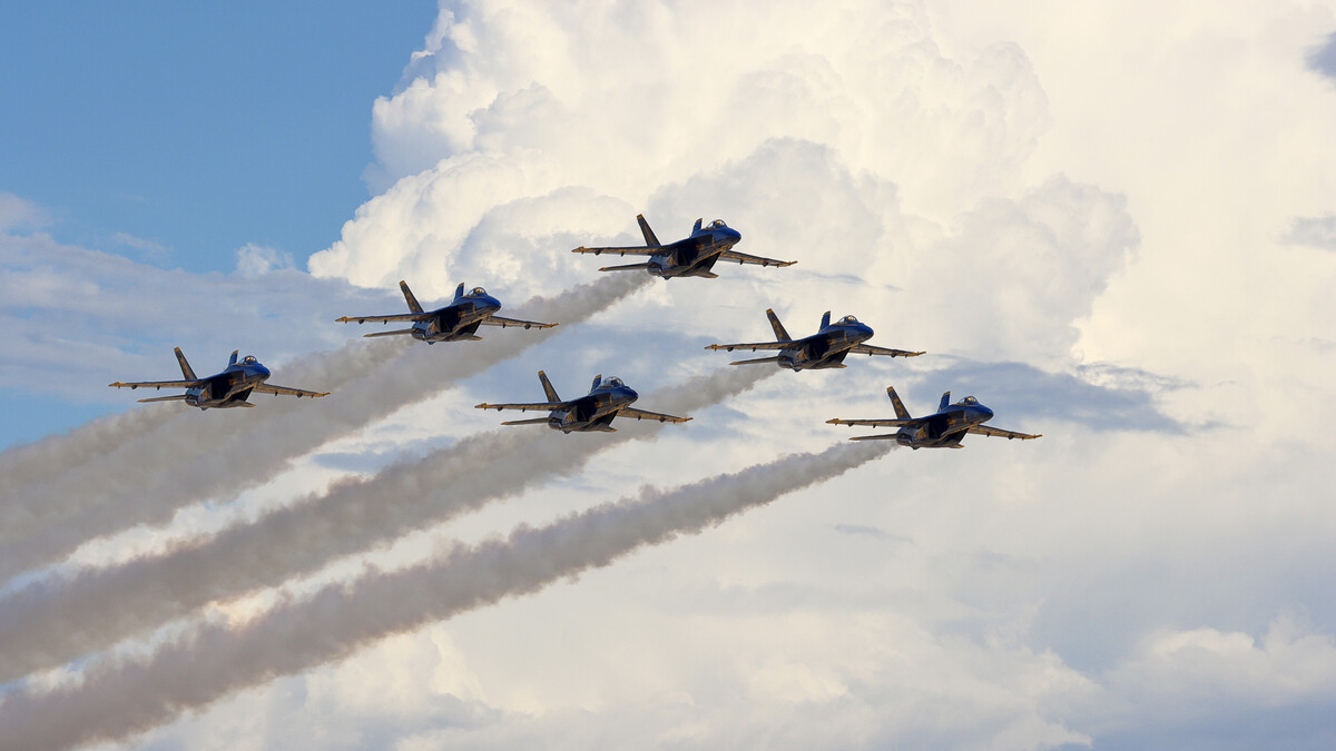 The Blue Angels sail through a cloudy sky, leaving behind trails from their planes.