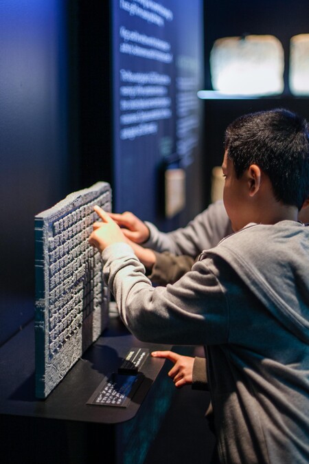 Young guest interacts with a hands-on exhibit featuring a stone tablet in Maya exhibition.