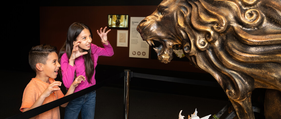 Kids make a lion face at the metal lion in the Da Vinci exhibition.